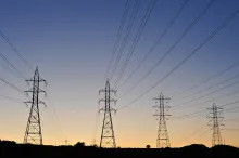 High-voltage electricity transmission towers and power lines silhouetted against a dusk sky.