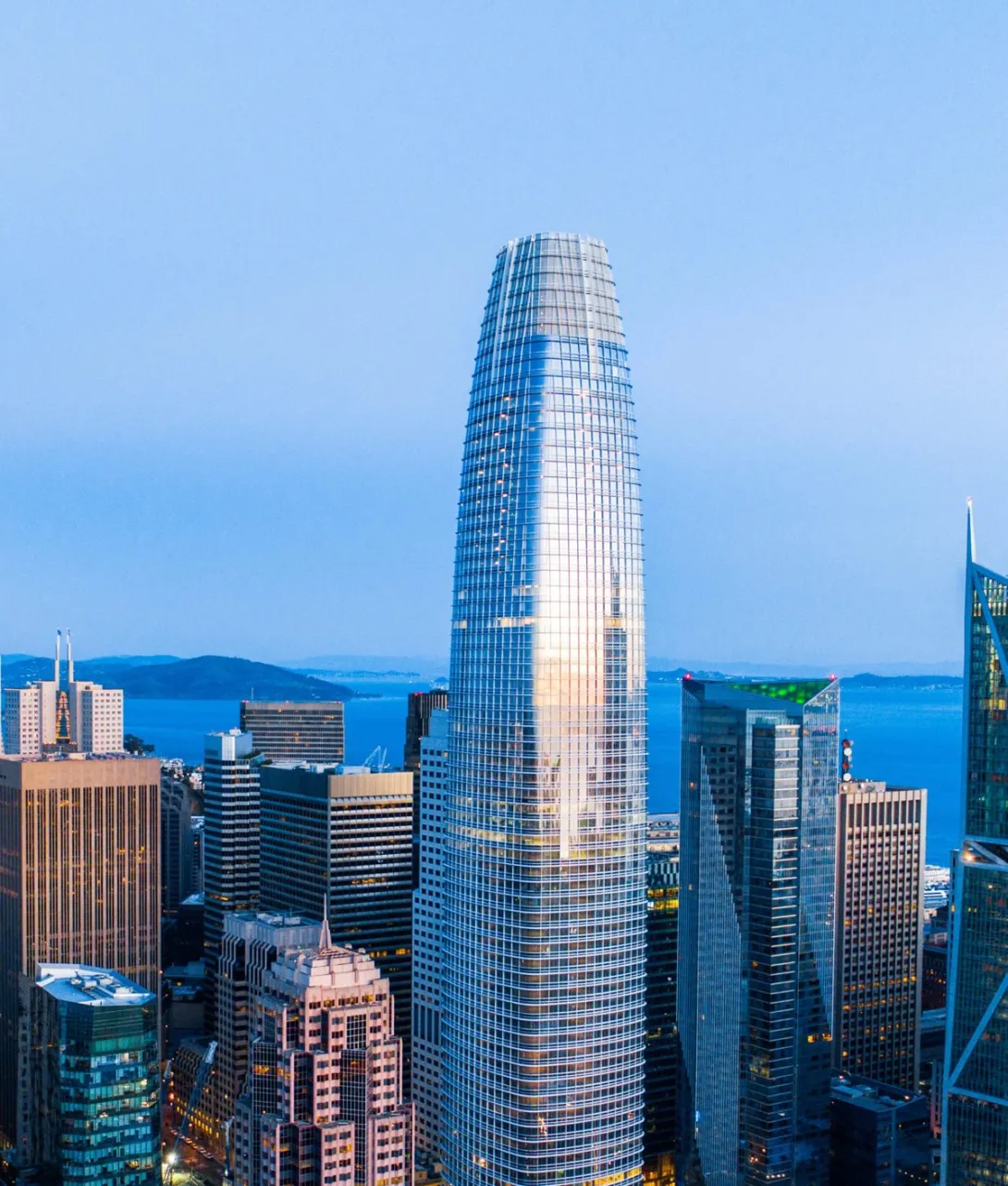 A photograph of Salesforce Tower rising above the downtown San Francisco skyline at dusk.