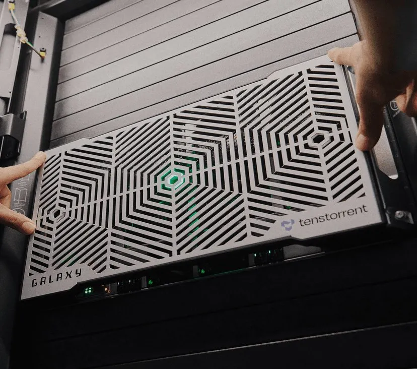 A technician's hands slide a Tenstorrent Galaxy AI server, with its geometric vented front panel, into a data center rack.